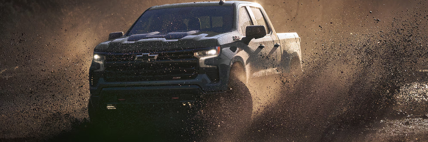 2026 Chevrolet Silverado LD driving off-road on a muddy terrain.