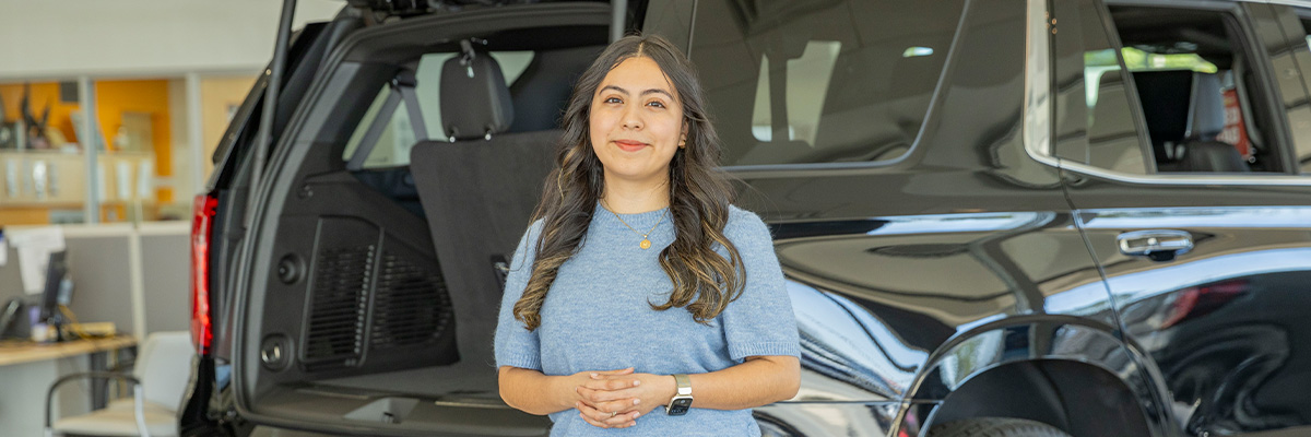 Spanish speaking dealership employee smiling standing in front of a vehicle