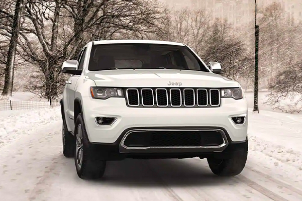 A front view of a Jeep Grand Cherokee Limited being driven on a snow-covered road in the city.