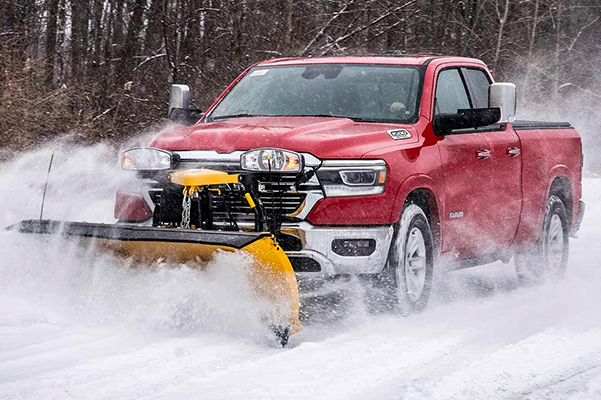 Ram 1500 clearing a road with a snowplow upfit attached to its front grille.