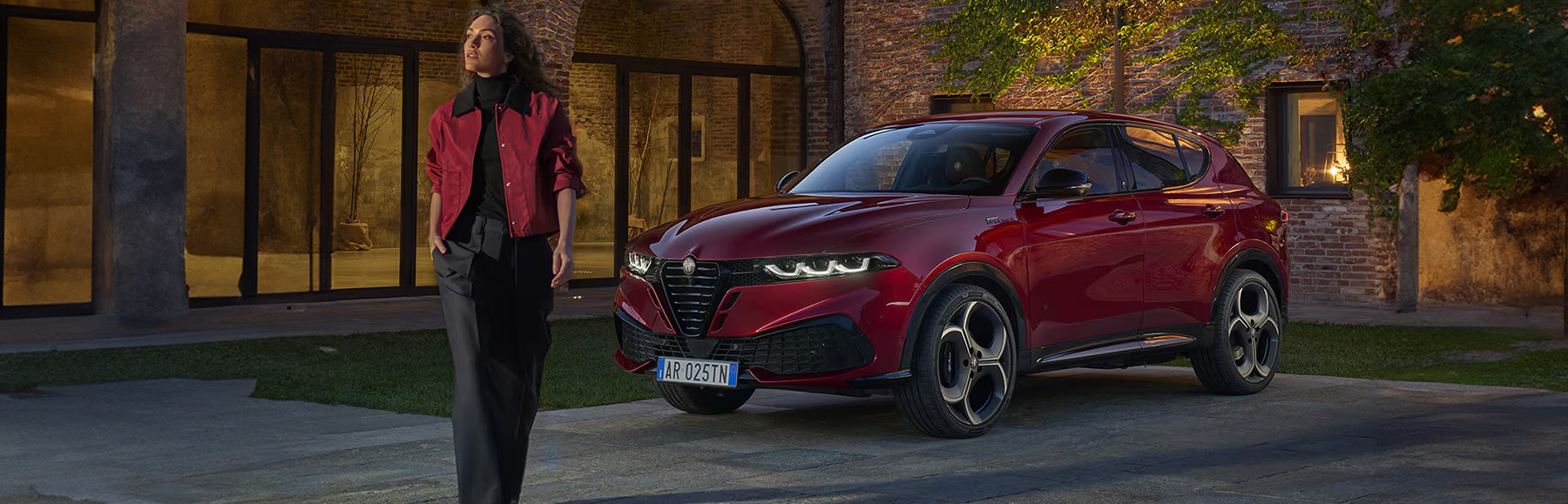 Stylish woman standing in front of a Alfa Romeo Tonale at night