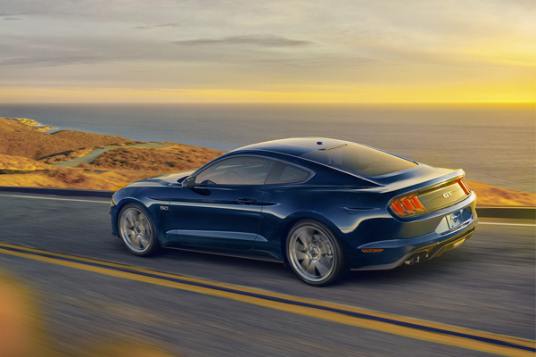 A 2021 Ford Mustang in Antimatter Blue being driven on the open road with an ocean in the background