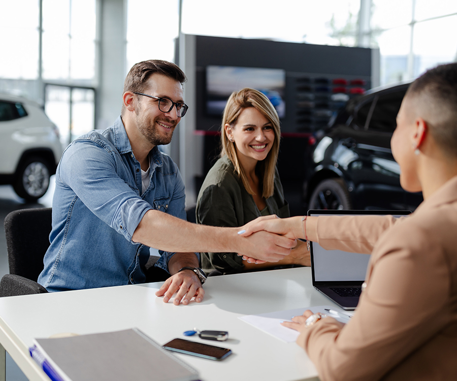 Male customer and female car dealer shaking hands at showroom.